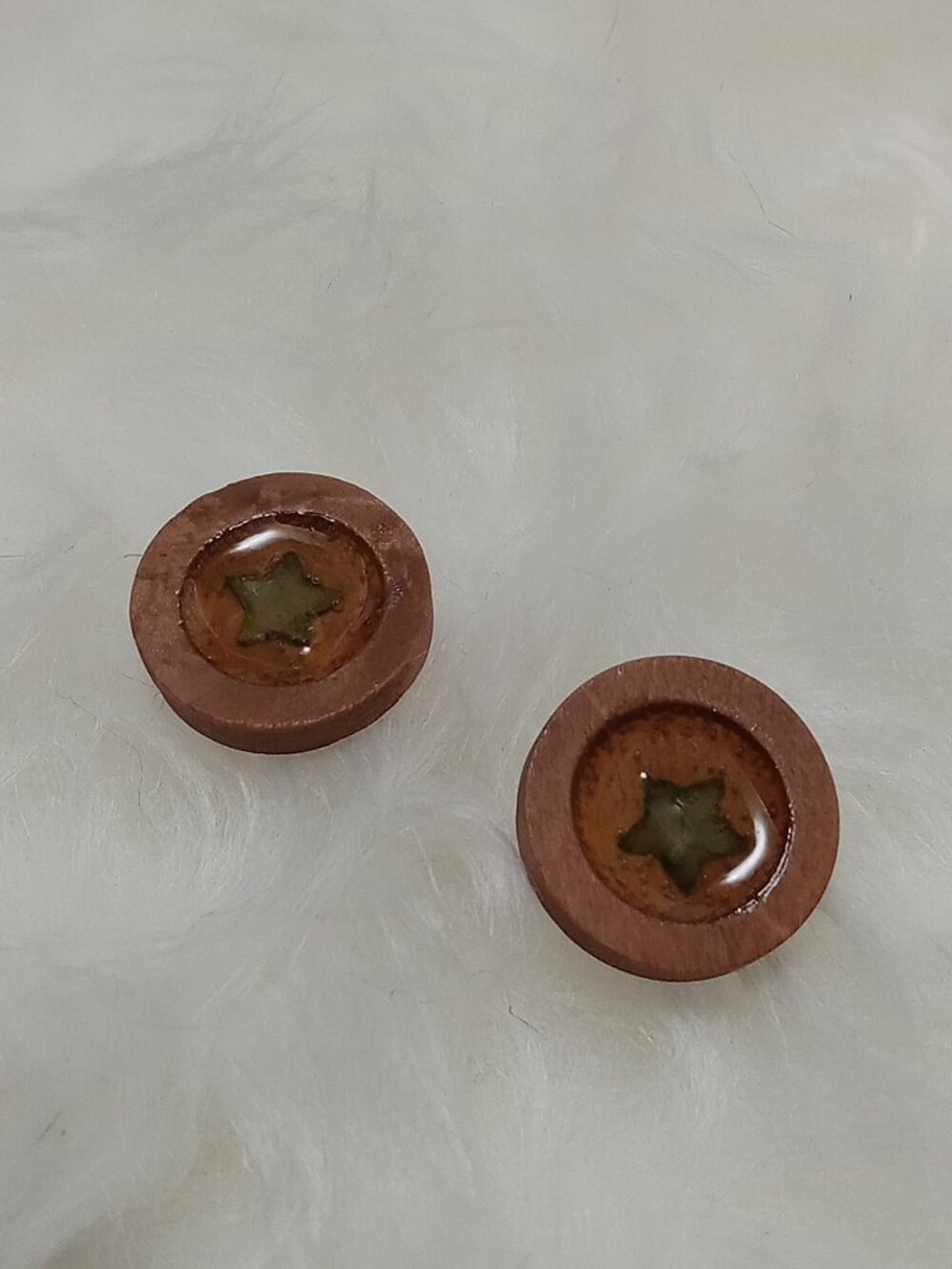 Handmade earrings on a wooden base with a piece of punched-out tree leaf